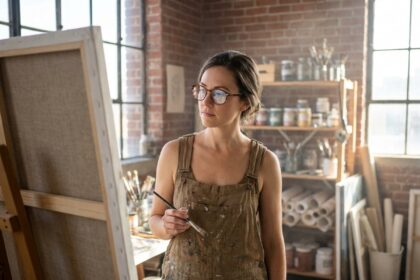Artiste peintre femme portant des lunettes rondes en écaille de tortue travaillant sur une grande toile dans son atelier bohème