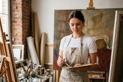 Jeune femme artiste peintre dans un atelier professionnel mélangeant des couleurs sur une palette en bois devant une grande toile